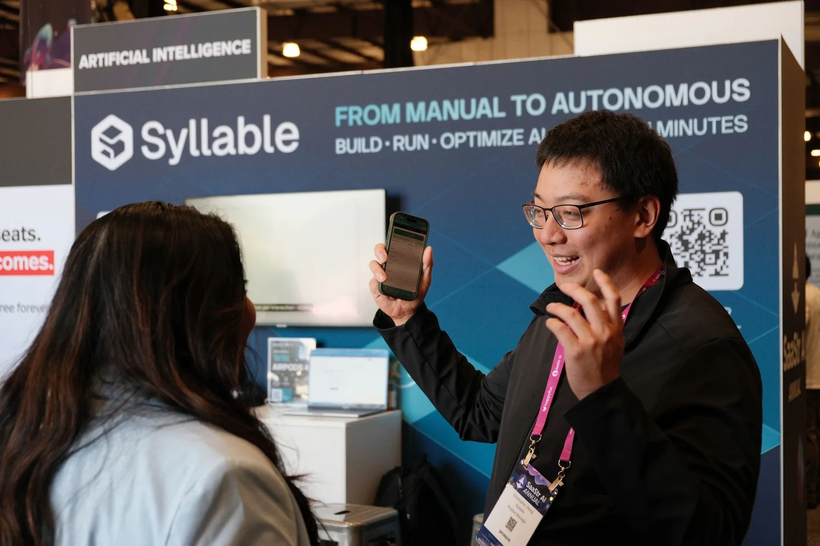A Syllable AI team member demoing an AI agent on a phone to an attendee at the booth